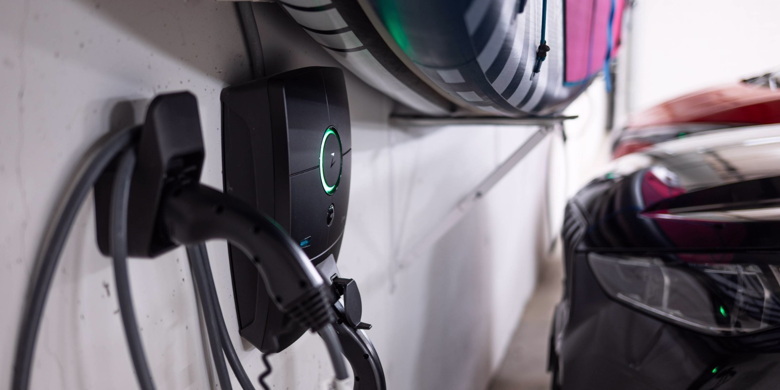 Ladestation mit eingestecktem Ladekabel neben einem parkierten Elektroauto