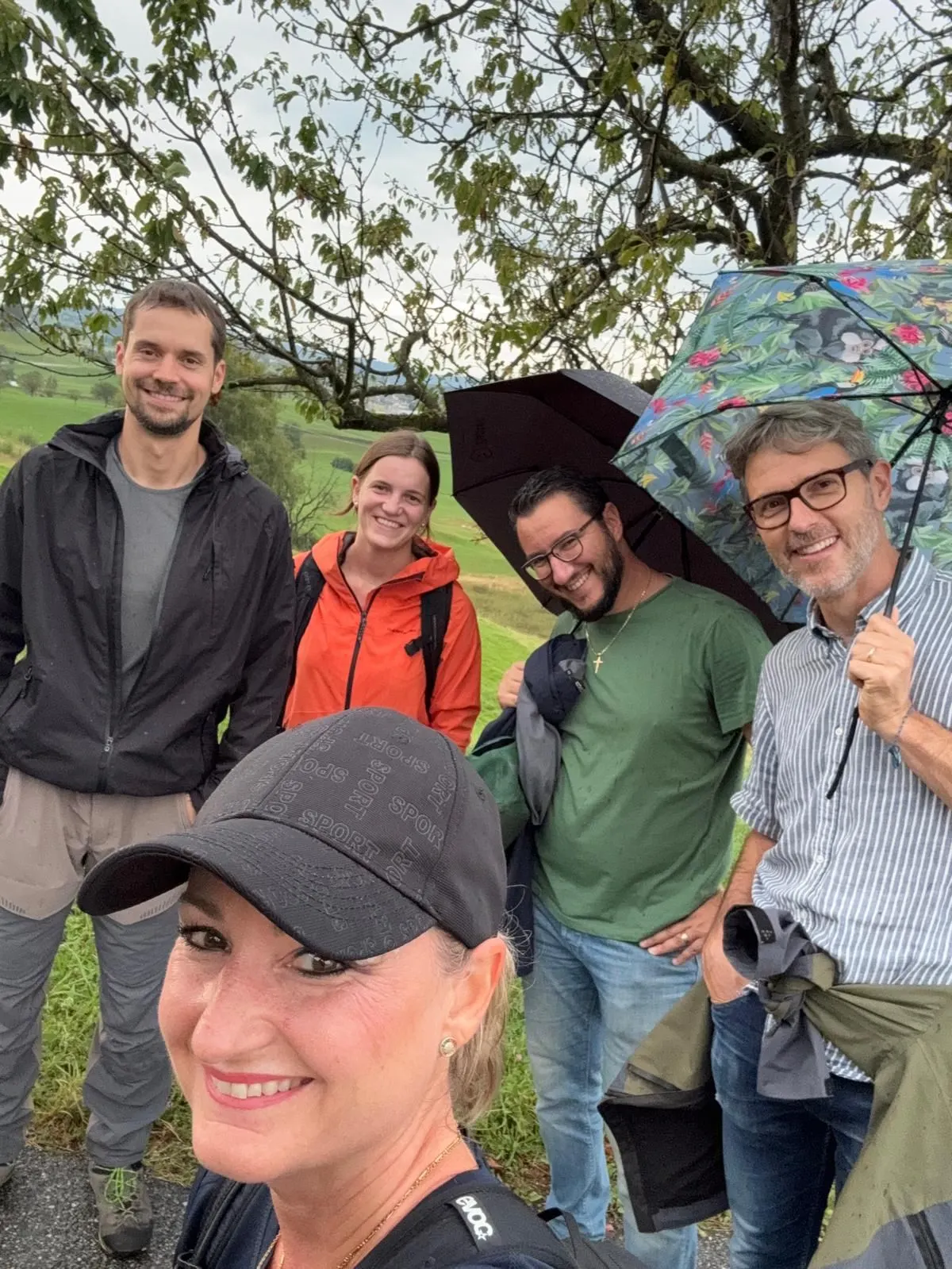 Sintio team group selfie outdoors in the rain with umbrellas