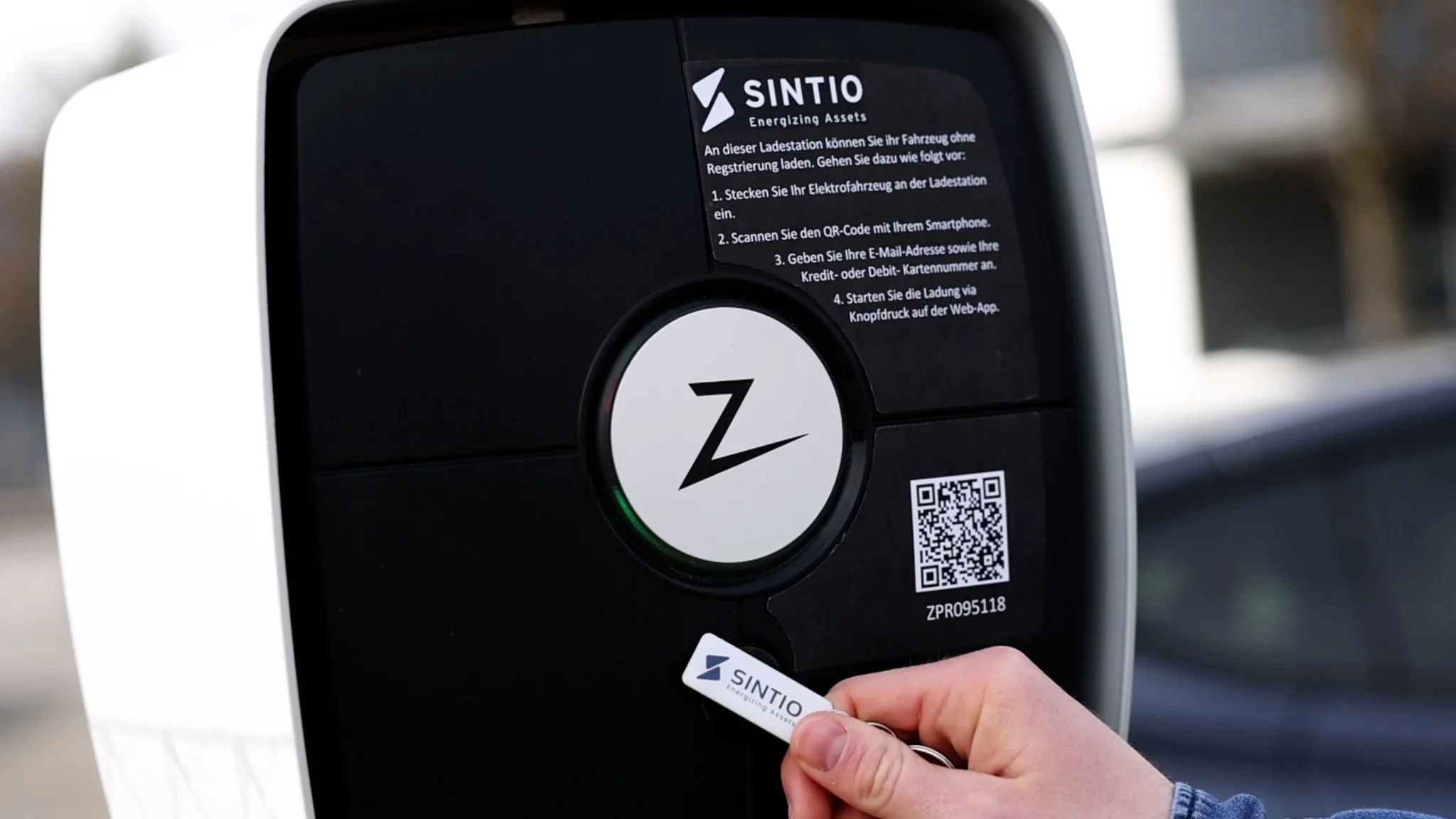 Hand holding a Sintio RFID tag near a charging station with QR code